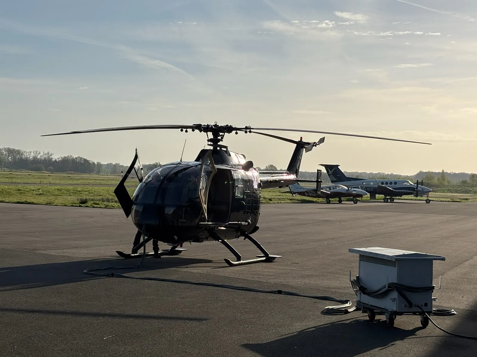Schwarze MBB BO105 mit geöffneten Türen und Bodengerät auf dem Vorfeld