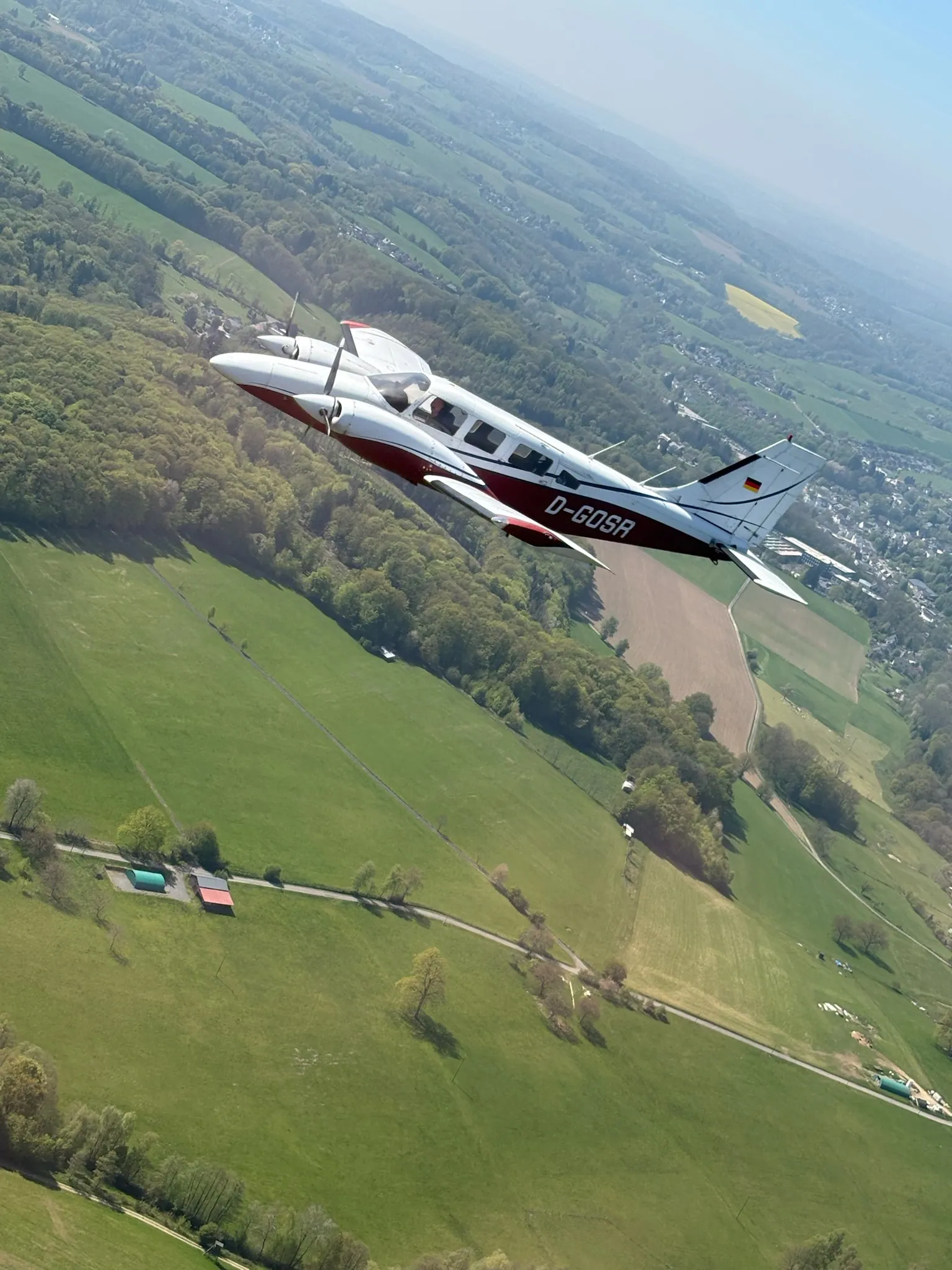 Piper Seneca D-GOSR im Kurvenflug über grüner Landschaft