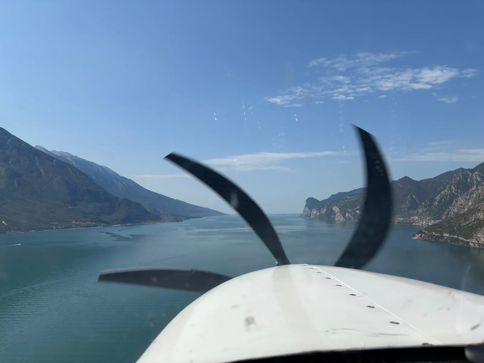 Blick über die Flugzeugnase auf einen See zwischen Bergen